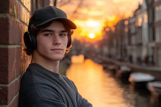 A young man leaning against a wall near the canals, wearing an oversized sweater and a baseball cap, listening to music through his vintage headphones. AI generative.
