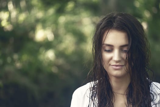Smiling attractive girl with wet long  hair is posing outdoors.  Edited as a cinematic photo. Horizontally.