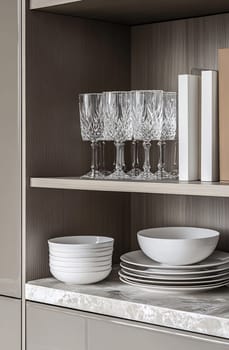 A neatly organized shelf showcases crystal glasses and various white dinnerware, creating a sophisticated dining atmosphere.