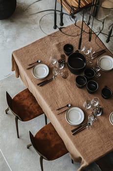A beautifully arranged dining table features dark dishware and glasses, set on a textured brown tablecloth in a cozy indoor setting.