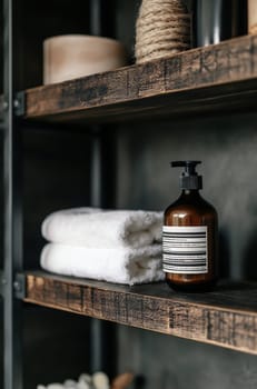 Soft towels sit beside a stylish dark bottle on well-crafted wooden shelves in a cozy bathroom setting.