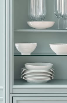 A sleek cabinet displays assorted white dinnerware, including bowls and plates, set against a soft-colored backdrop.