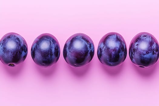 Five ripe plums are neatly arranged on a vibrant pink background, showcasing their smooth skin and rich color.