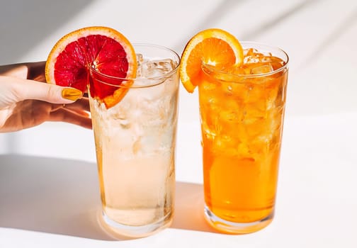 Two tall glasses filled with ice-cold citrus drinks, one garnished with blood orange and the other with orange slices.