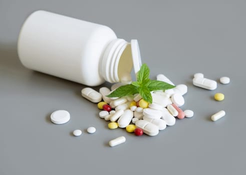 Mixed medical capsules and pills and a bottle, green mint leaves on themon grey closeup. Medicinal treatment. Taking dietary supplements and vitamins
