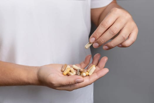 Woman holding in hands beige medical capsules closeup over white shirt and taking one capsule with fingers. Alternative herbal products for health care