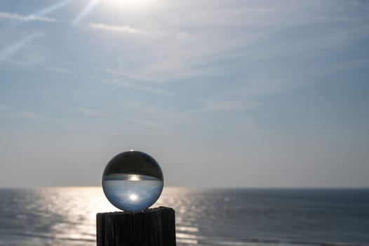 Glass ball lies on a wooden post, in the ball the sea, the sun and the blue sky are reflected