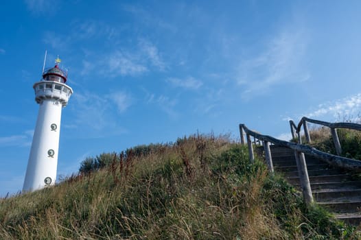 The approx. 28 m high white lighthouse J.C.J. van Speijk in Egmond aan Zee, North Holland, Netherlands, in the sand dunes with beach grass and a staircase with wooden railing