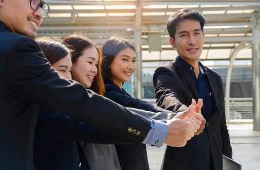 Business people team in black suits standing in city outdoors and showing thumbs up. One of them holding laptop and looking at camera. Teamwork, cooperation and business successful concept