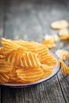 Crispy potato chips on plate on a wooden table.