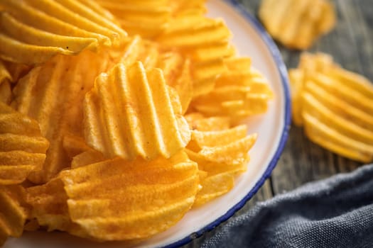 Crispy potato chips on plate on a wooden table.