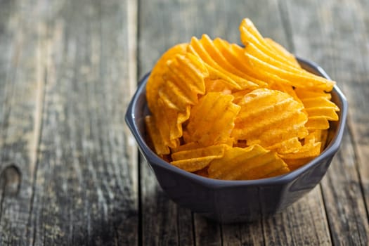 Crispy potato chips in bowl on a wooden table.