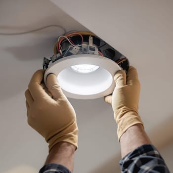 Hands wearing gloves install an LED ceiling light, focusing on the intricate wiring and secure attachment.