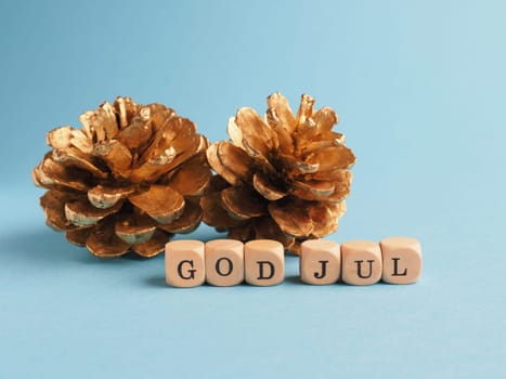Golden pine cones with wooden blocks and the words God Jul, Scandinavian Merry Christmas on a blue background