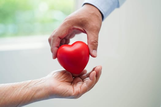 Asian elder senior woman patient holding red heart in hospital.