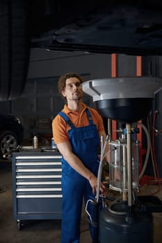 Professional automotive engineer working at car repair station with broken custom vehicle lifted on elevator machine for changing oil