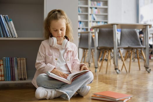 Cute curious little girl child reading book on floor of modern city bookstore. Kid reading paper book while spending time in public library for children. Education concept