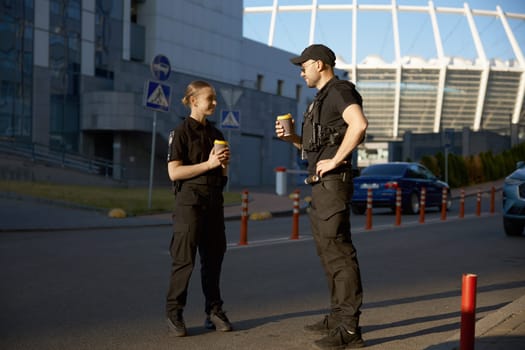 Cheerful patrol officers talking together drinking coffee having work day break. Nice conversation and friendly relationship at job