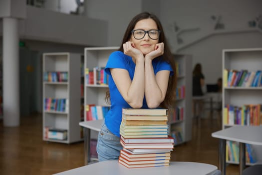 Young woman with huge stack of paper book feeling overloaded standing over bookstore interior background