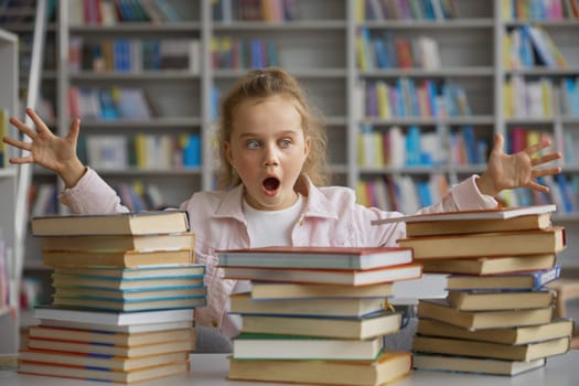 Shocked little school girl with overwhelmed face looking at stack of textbooks on table in library or bookstore