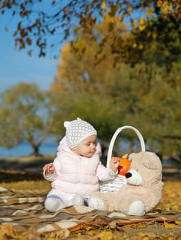 A joyful baby happily playing with a soft teddy bear surrounded by colorful and bright autumn leaves