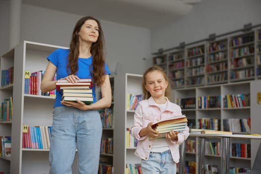 Happy family doing shopping at bookstore. Mother and daughter carrying books in stack preparing for studying