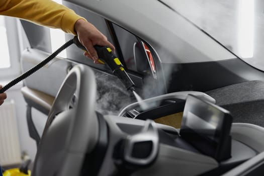 Steam cleaning of car interior innovative technology with minimal time costs. Closeup view on male master hands using professional equipment with special nozzle for cleansing dashboard