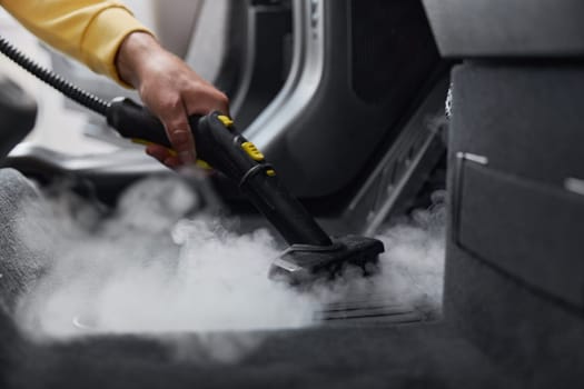 Master using cleaning properties of steam for cleansing car interior from various contaminants. Closeup view on special nozzle