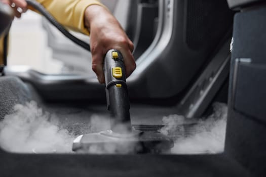 Service worker using cleaning properties of steam for cleansing car interior from various contaminants. Closeup view on special nozzle