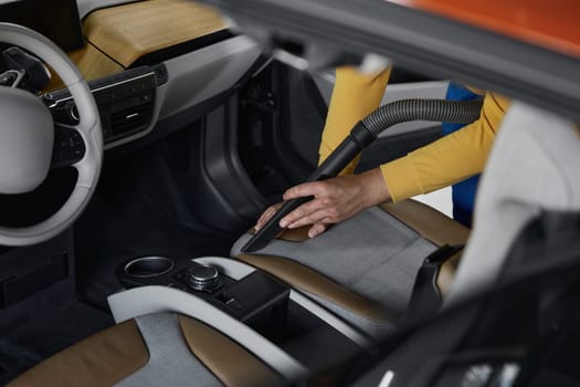 Car service male worker cleaning front seats from dust and dirt using vacuum cleaner professional electric appliance