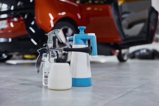 Detergent, antiseptic, duster spray kit for car cleaning and detailing service in garage workshop with shiny automobile cropped shot on background