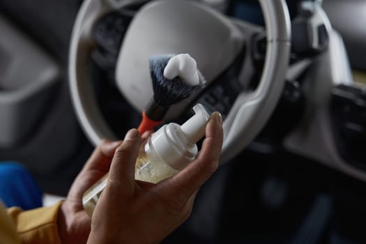 Closeup view on male master hand using foam in spray bottle applying detergent on brush to provide professional car cleaning and valeting service