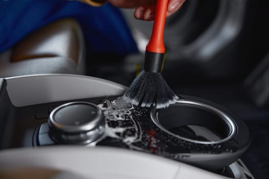 Closeup male worker cleaning car interior with duster brush and detergent foam. Garage wash and detailing service concept