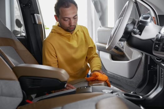 Detailing worker washing leather car interior parts with rag napkin and brush at professional auto service closeup