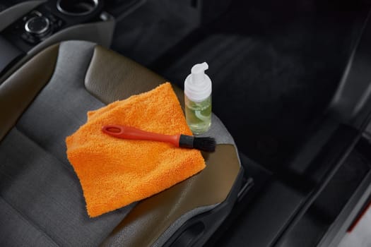 Cleansing brush towel and detergent in disinfectant spray bottle on front passenger seat high angle view closeup. Car detailing concept