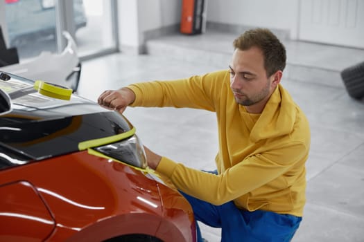 Man worker using masking tape to protect painted parts of body near headlights before polishing procedure. Car wash service concept