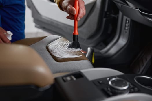 Male worker washing leather car interior parts with rag napkin and brush at professional auto service closeup