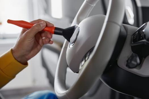 Closeup male autoshop worker hand cleaning steering wheel with detergent foam and brush. Car cleansing and detailing service