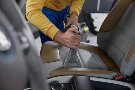 Man worker cleaning car interior with washing vacuum cleaner using special nozzle for hard to reach places. Auto cleaning and detailing service