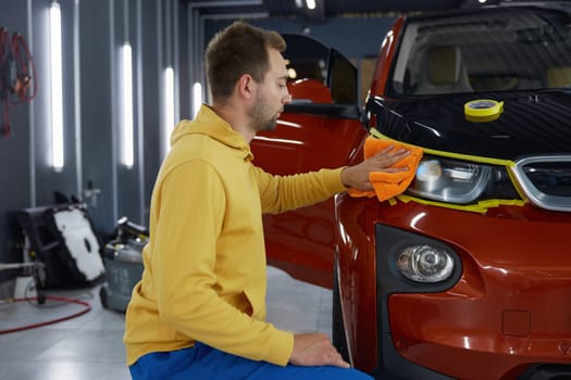 Service technician polishing headlamps using manual power rotary grinder tool with special nozzle while working at car garage workshop