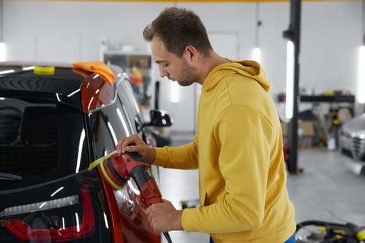 Auto master using rotary grinder for polishing car body parts. Automotive detailing service