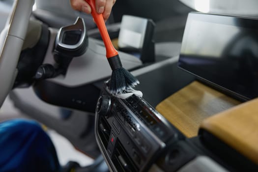Closeup male worker cleaning car interior with duster brush and detergent foam. Garage wash and detailing service concept
