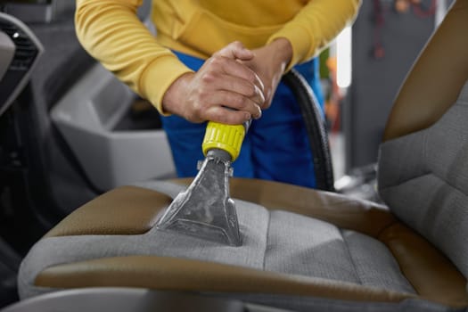 Cleaning car interior with washing vacuum cleaner using special nozzle for hard to reach places. Auto cleaning and detailing service