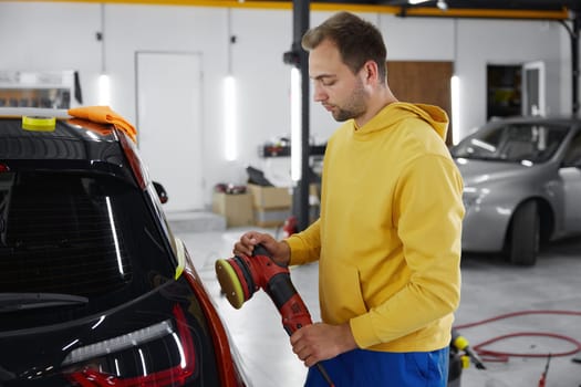 Cropped shot of auto master using rotary grinder for polishing car body parts. Automotive detailing service