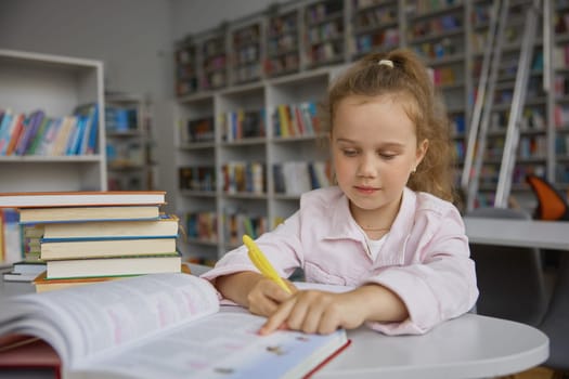 Little cute smart preschool girl child writing while doing homework. Clever pupil studying at library over bookshelves background