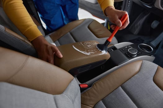 Autoshop worker cleaning car interior with detergent foam and brush. Car cleansing and detailing service