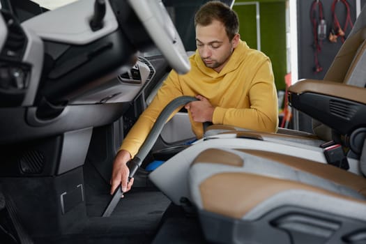 Male master vacuuming car interior from dust using professional equipment. Car-wash service concept
