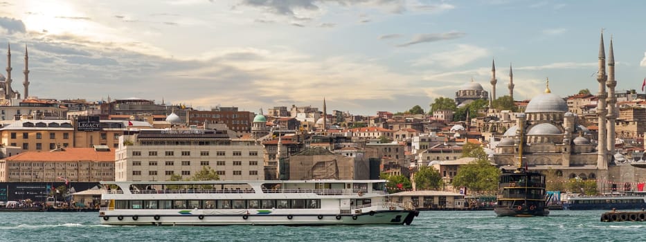 Istanbul, Turkey - May 13, 2023: A ferry cruises along the Bosphorus Strait as the sun sets, highlighting Istanbul's iconic skyline filled with historical architecture and minarets