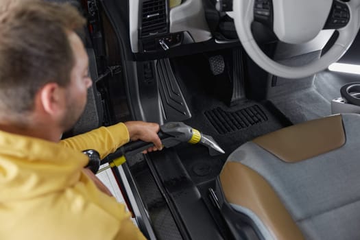 Car wash service worker vacuuming dust and dirt form back passenger seats applying professional equipment