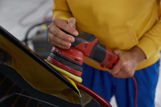 Service man providing professional detailing service in car studio. Man mechanic polishing automotive body parts with electric orbital polisher power machine